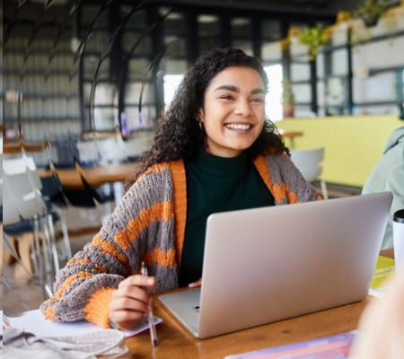 A young teen girl in an orange and grey sweater working on an online class for Pearson Online Academy