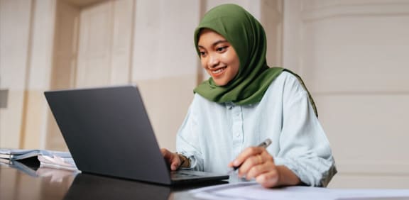 A young Muslim woman in a green hijab smiling taking a class for Pearson Online Academy. 