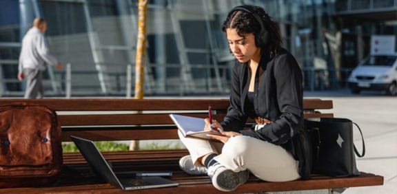 Young teen student sitting on a park bench working on an online assignment for Pearson Online Academy. 