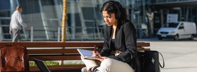 High  school online private school student attends LiveLesson session sitting on a park bench outside - Pearson Online Academy